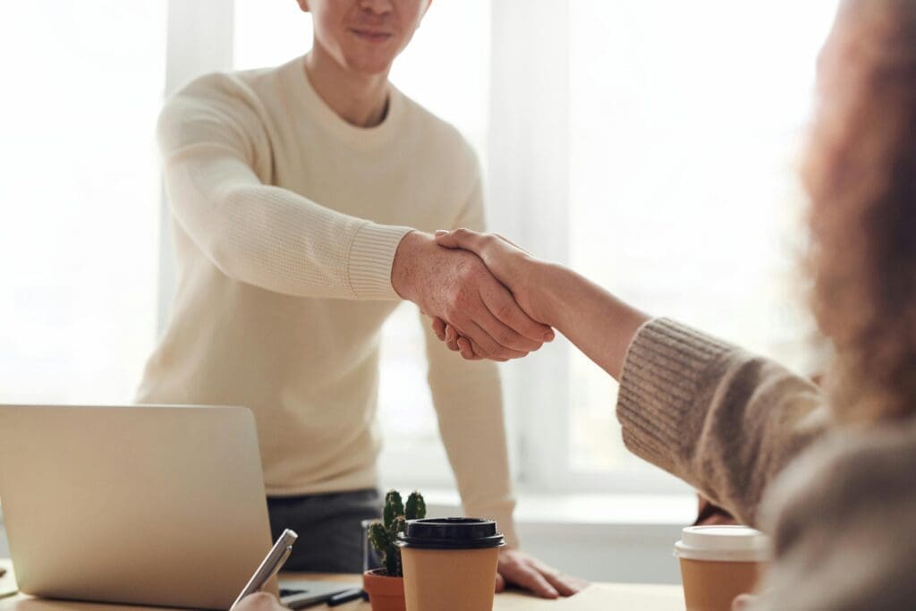 Poignée de main entre deux personnes dans un environnement professionnel, avec ordinateur portable et café sur la table